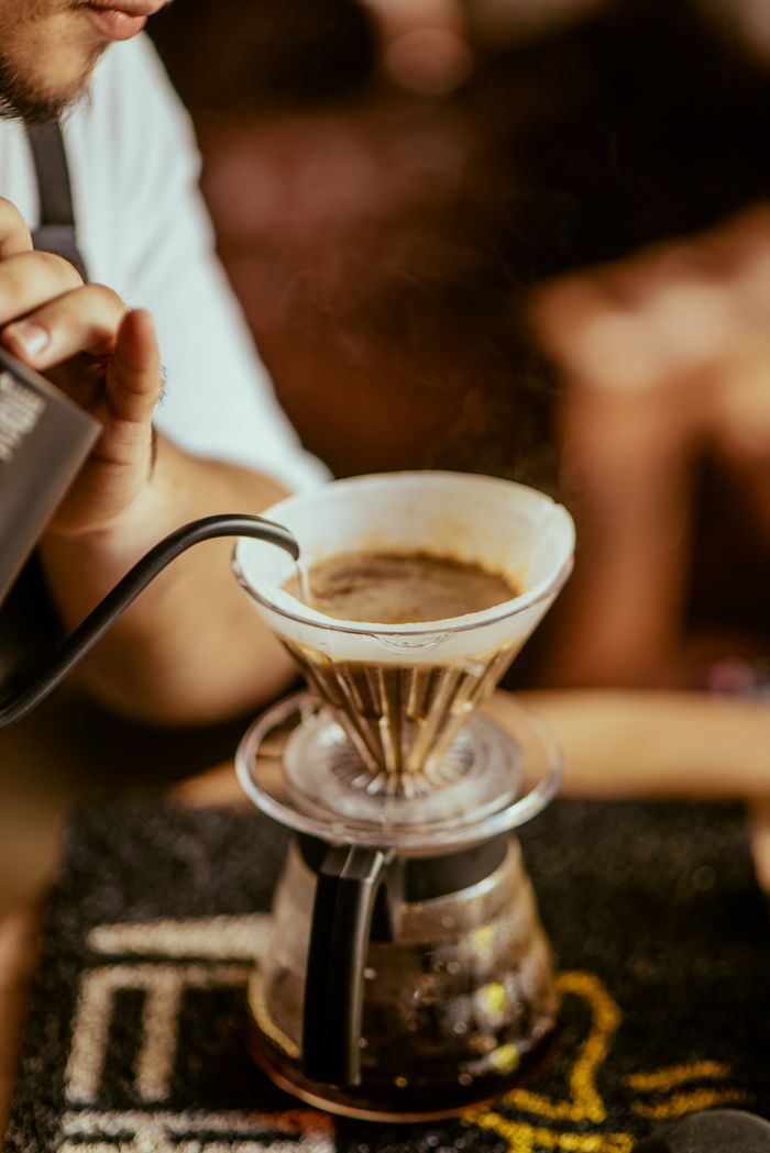 why-choose-us Person pouring hot water through a dripper for manual coffee brewing.