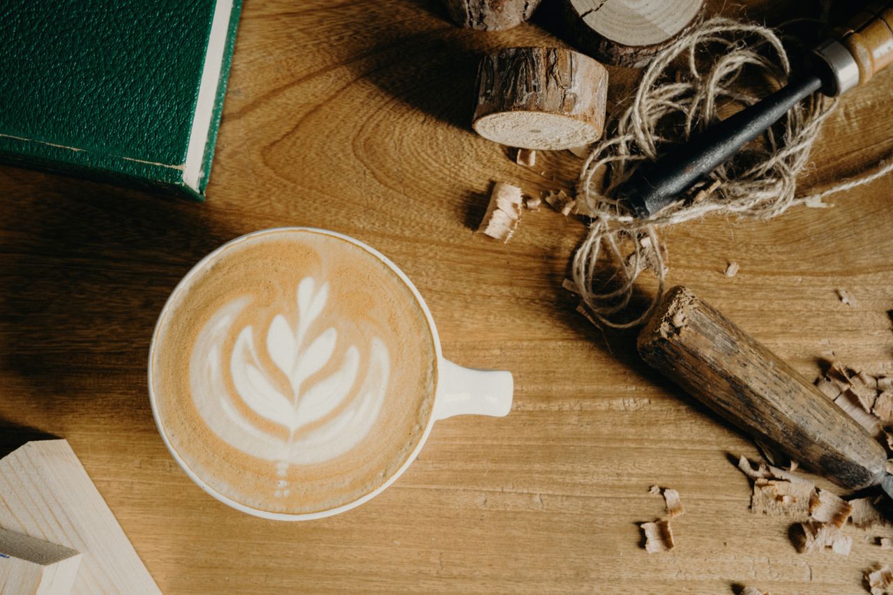 services-06 A beautifully crafted latte with latte art on a wooden table surrounded by woodworking tools and a book.