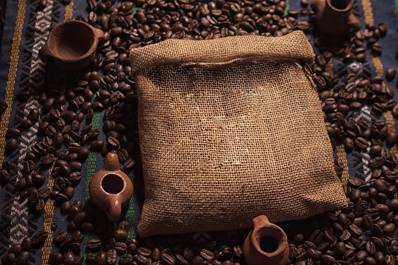 about-us Burlap sack filled with coffee beans, surrounded by pottery and traditional textile.