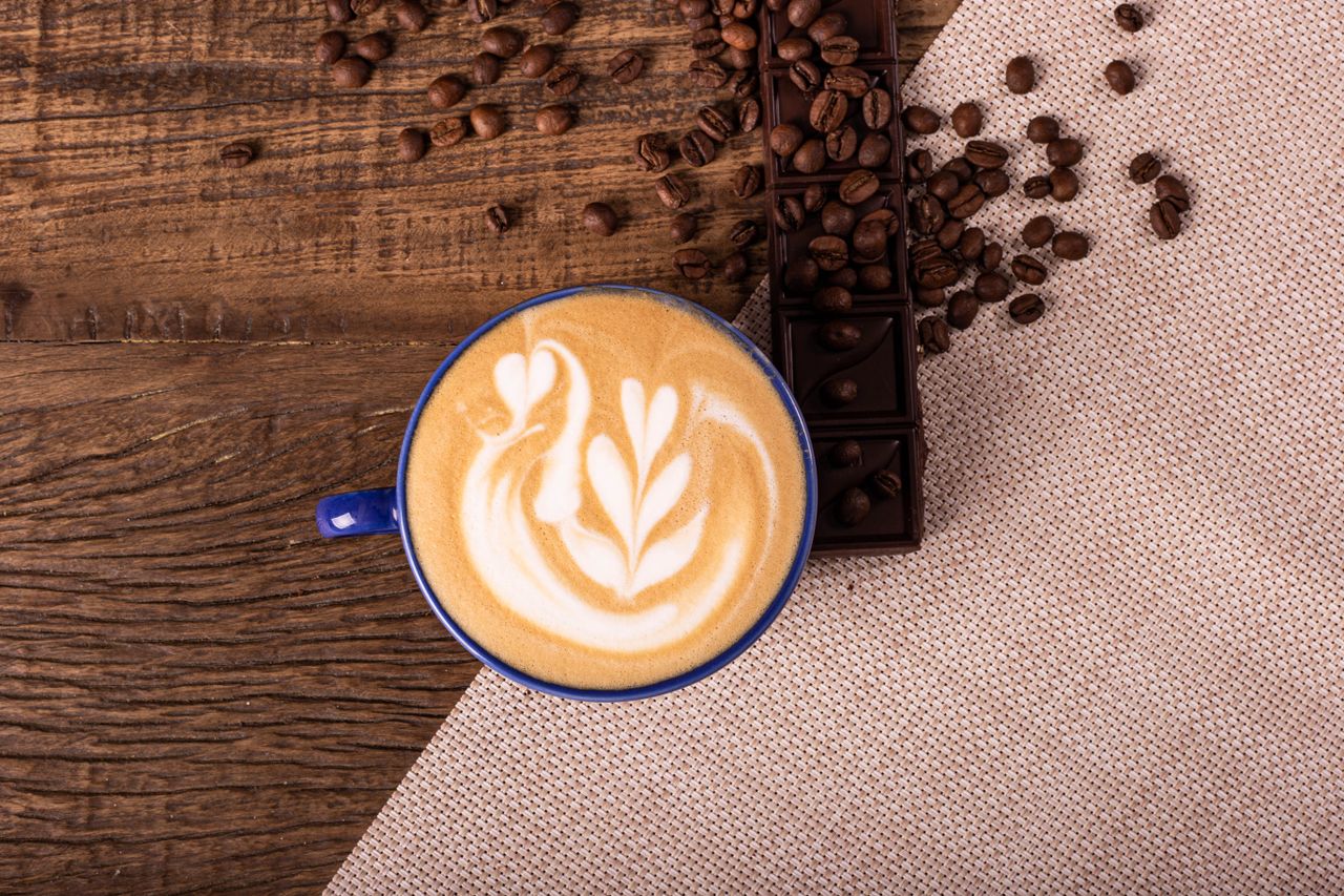 services-05 Overhead view of a latte with swan latte art, surrounded by coffee beans and chocolate on rustic wood.
